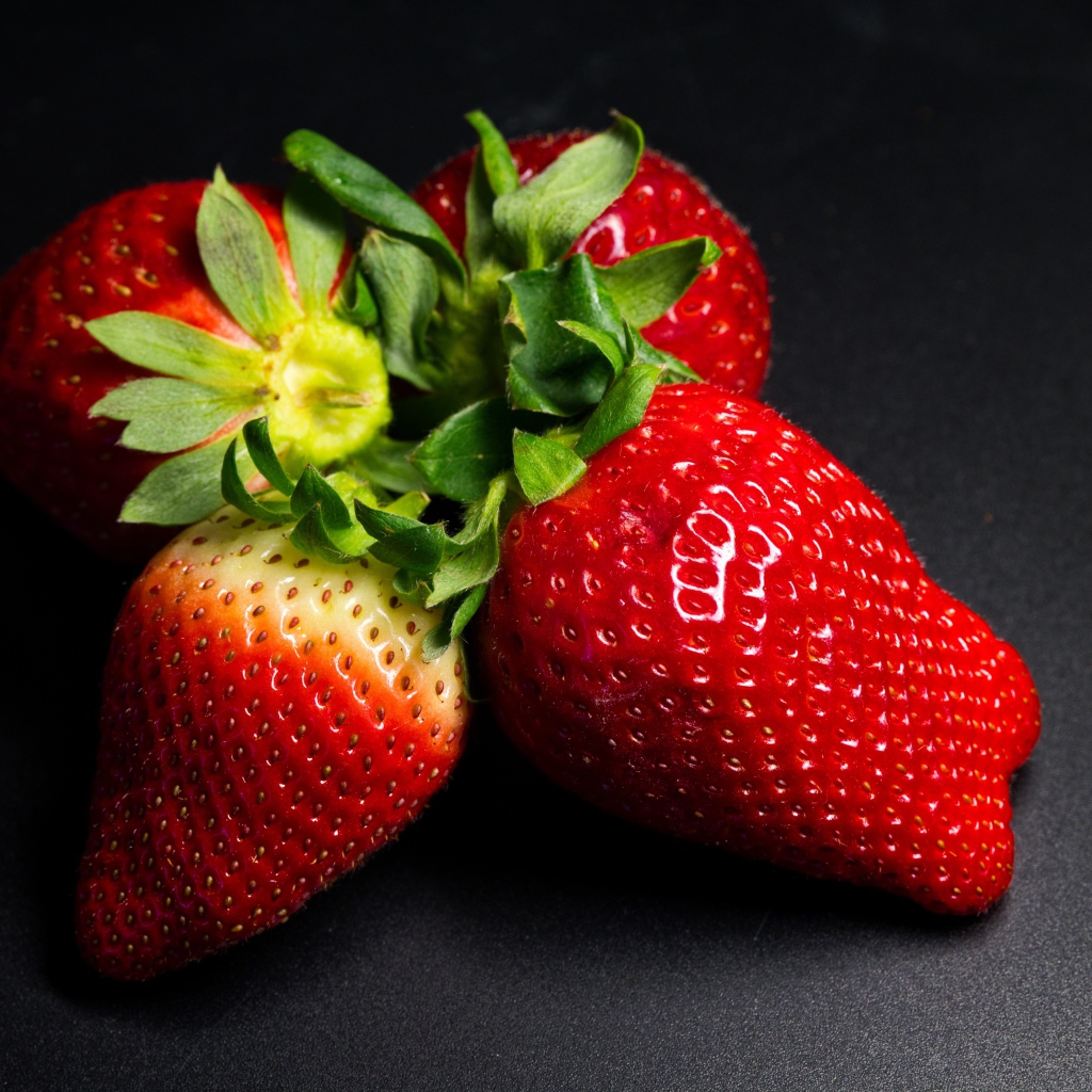 Четыре спелых красных ягоды клубники на черном столе 