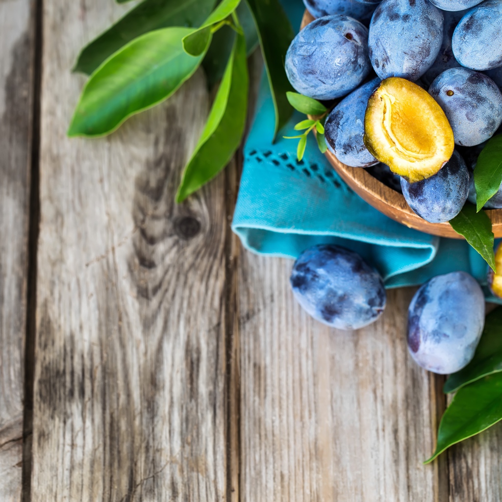 Свежие синие сливы с зелеными листьями на столе 
