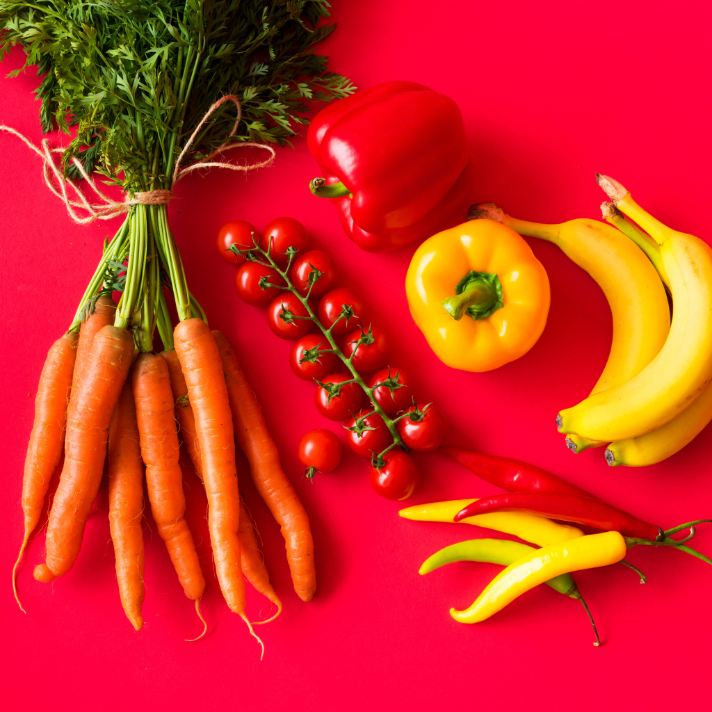Свежие морковь, помидоры, перец и бананы на красном фоне