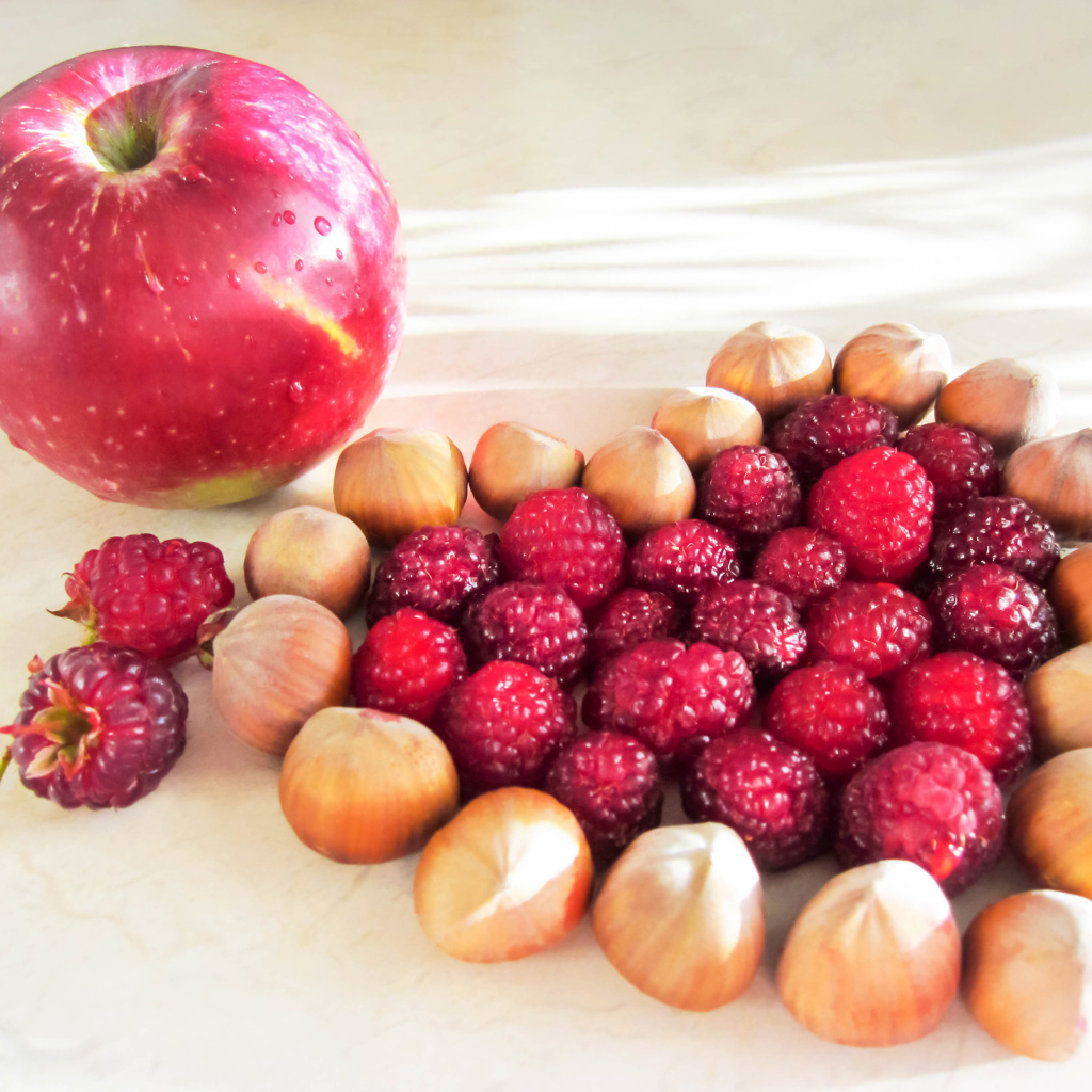 Сердце из лесных орехов и малины на столе с красным яблоком