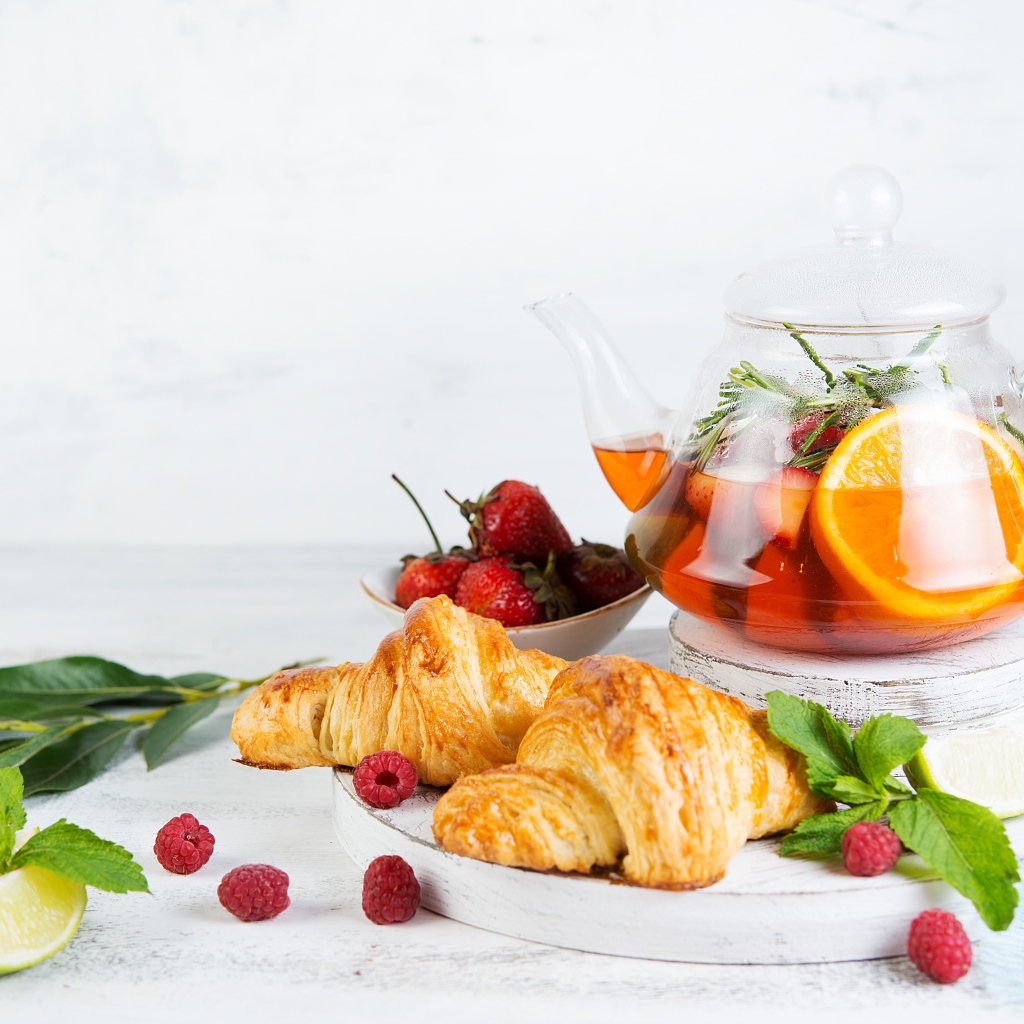 Чайник с лимоном и клубникой на столе с круассанами 