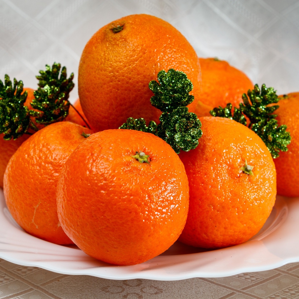 Много оранжевых мандаринов на тарелке с шишками