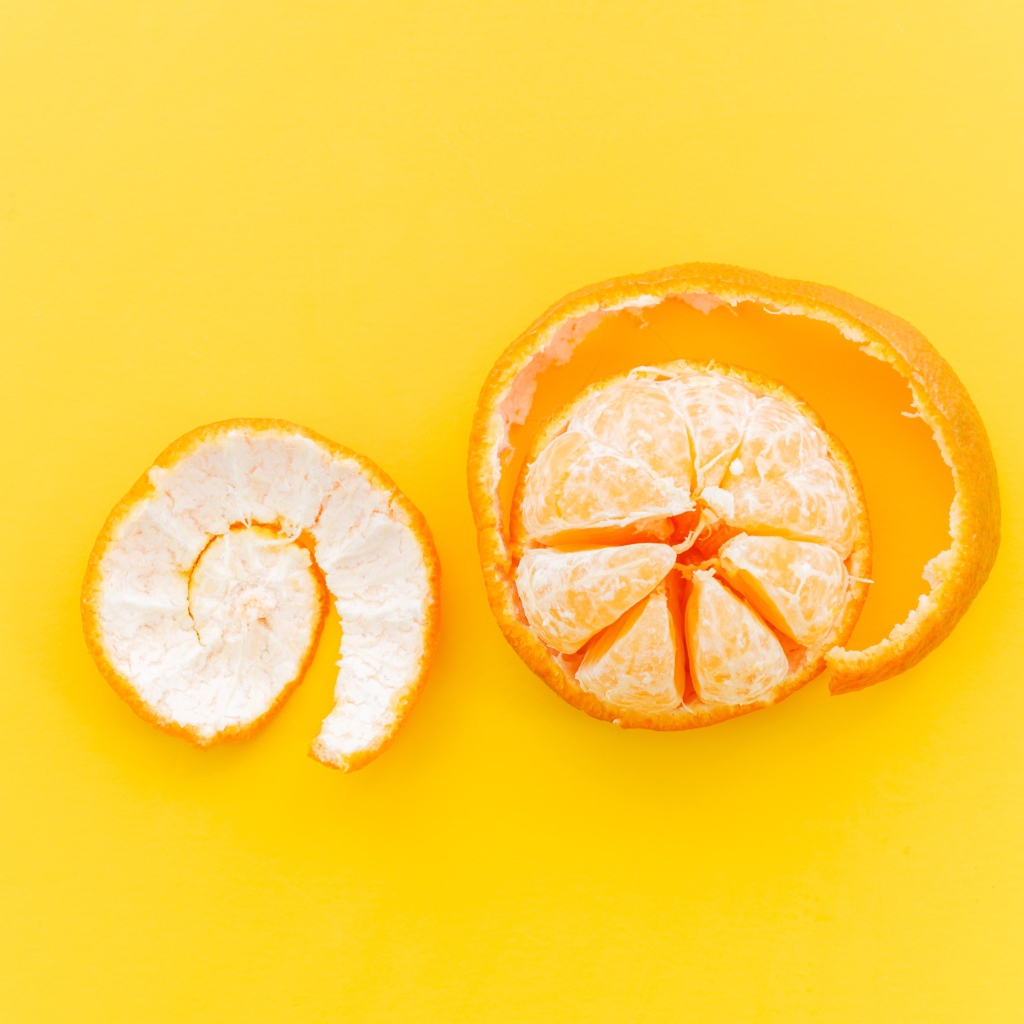 Очищенный мандарин с кожурой на желтом фоне 