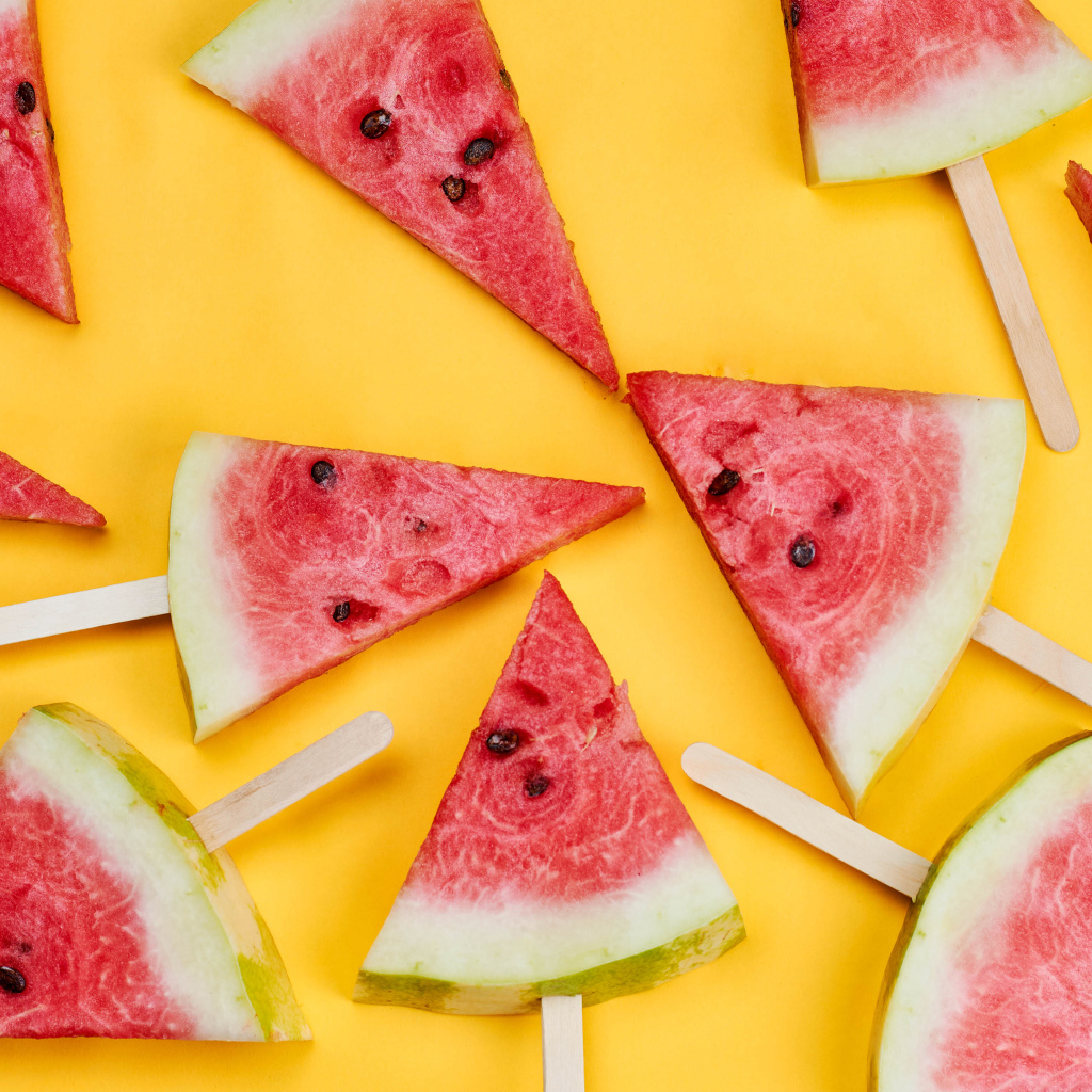 Pieces of watermelon on sticks on yellow background