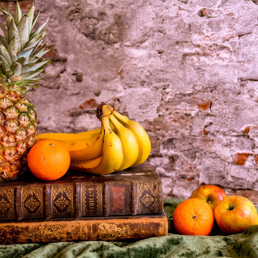 Ананас, бананы, апельсин и яблоки лежат на столе с книгами
