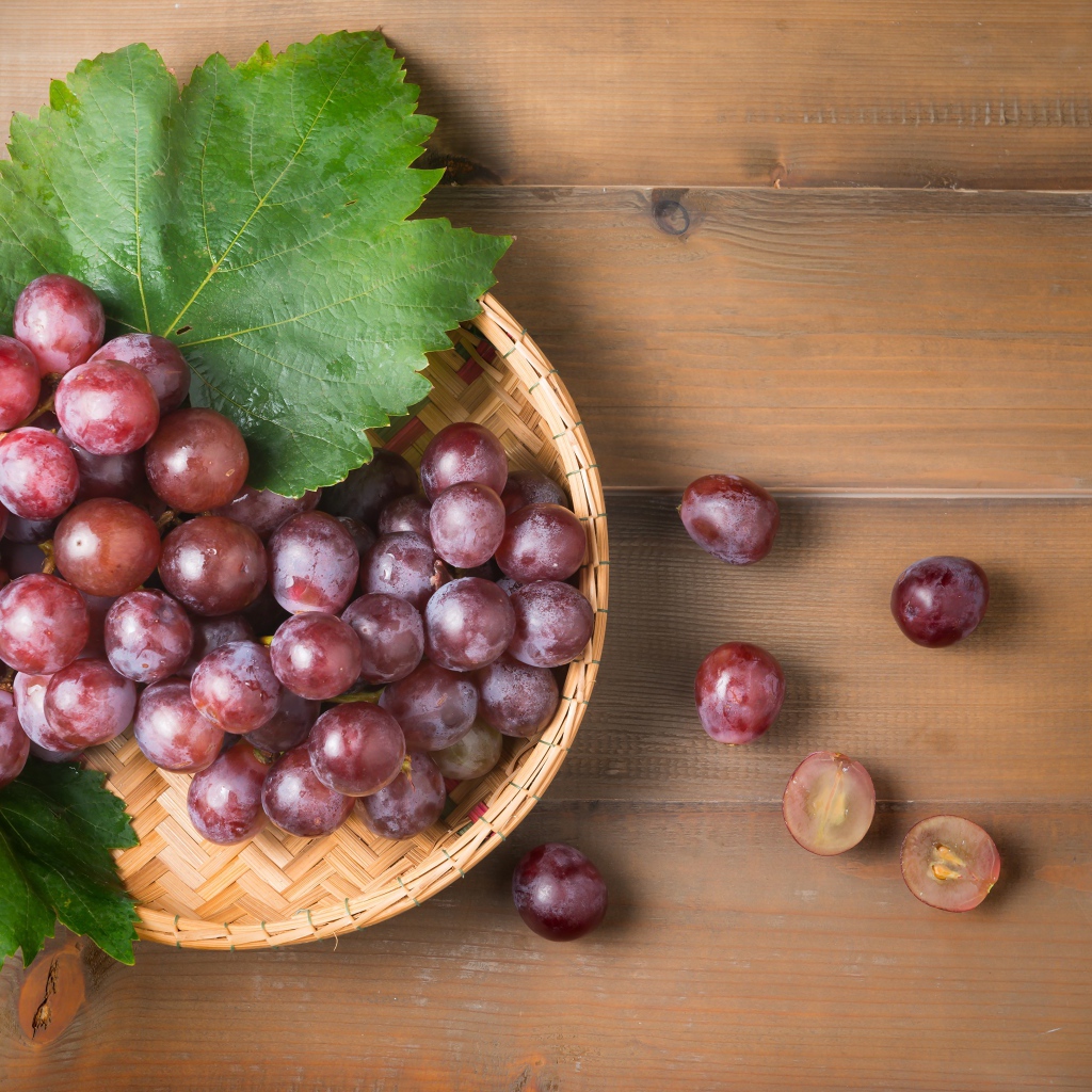 Розовый виноград с зелеными листьями на деревянном столе 