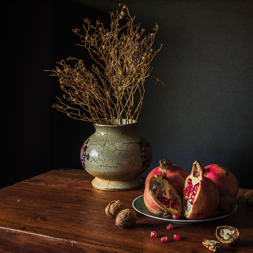 Красный гранат на столе с грецкими орехами и сухой веткой в вазе