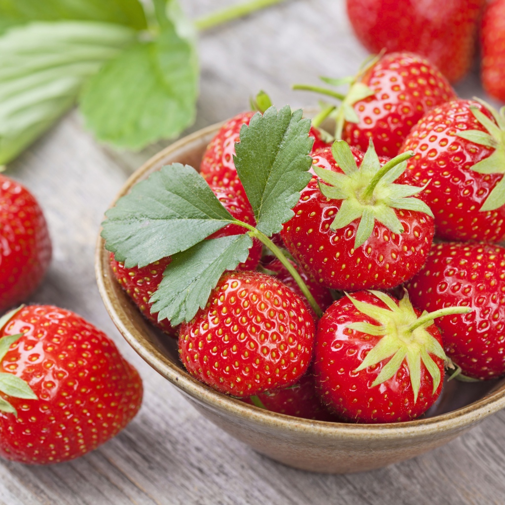 Красная спелая сладкая клубника в тарелке с зелеными листьями