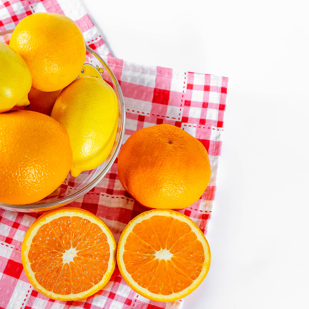 Спелые апельсины и лимоны в стеклянной миске на столе