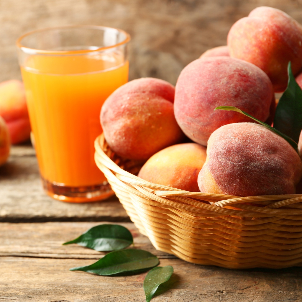Спелые персики в корзине на столе с соком