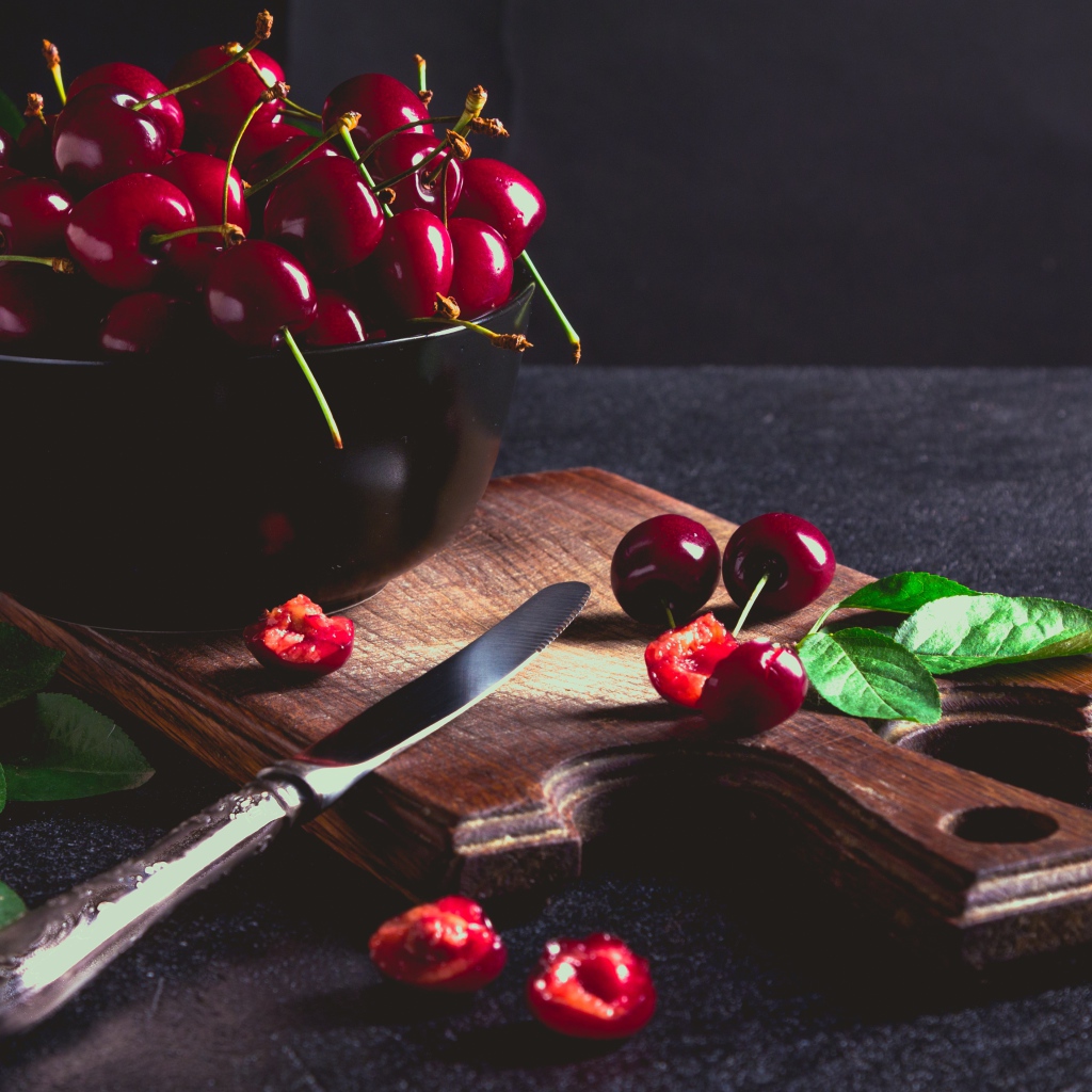 Спелые красные черешни на разделочной доске на столе 