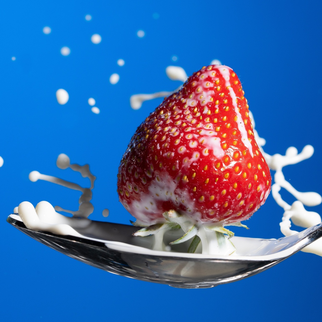 Ripe red strawberries in a spoon of milk on a blue background