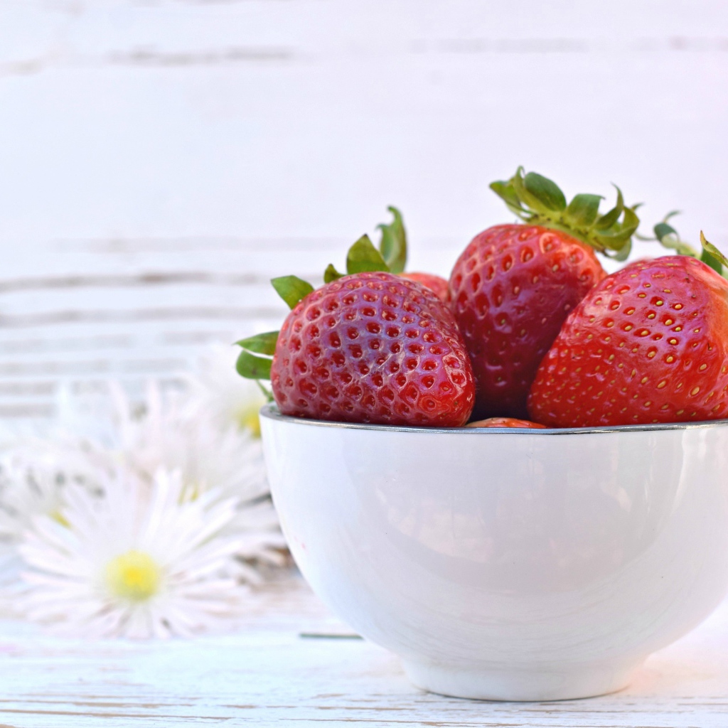 Спелая клубника в белой миске на столе с ромашками