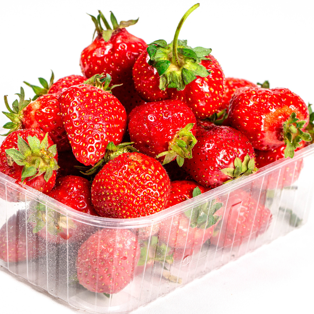 Спелая вкусная клубника в пластиковом контейнере на белом фоне