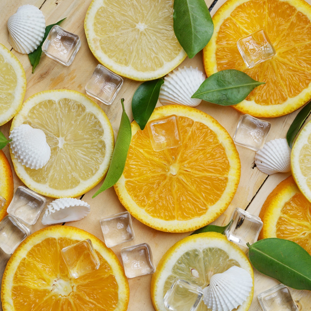 Кусочки апельсина и лимона на столе с кубиками льда и ракушками