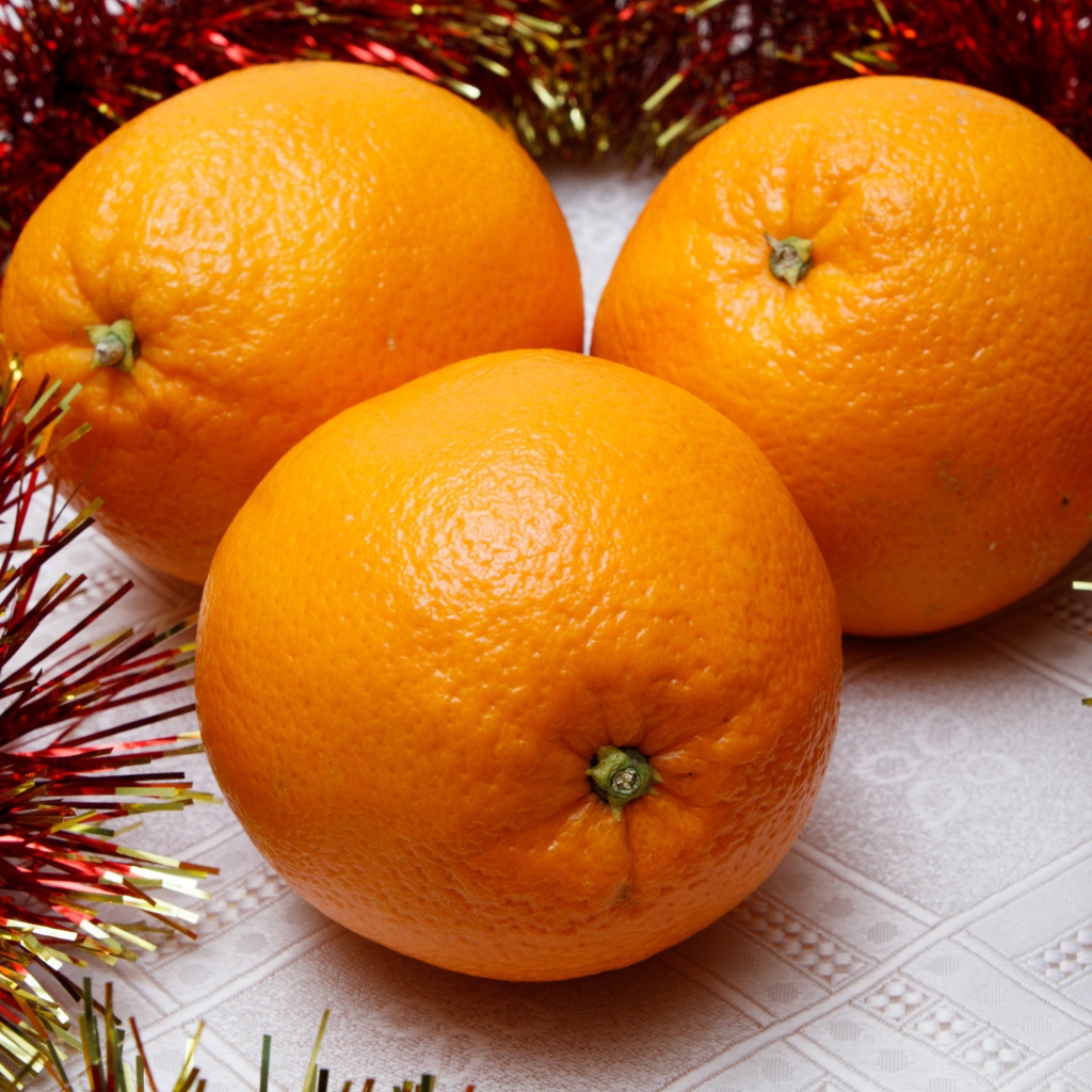 Три больших апельсина на столе с мишурой 