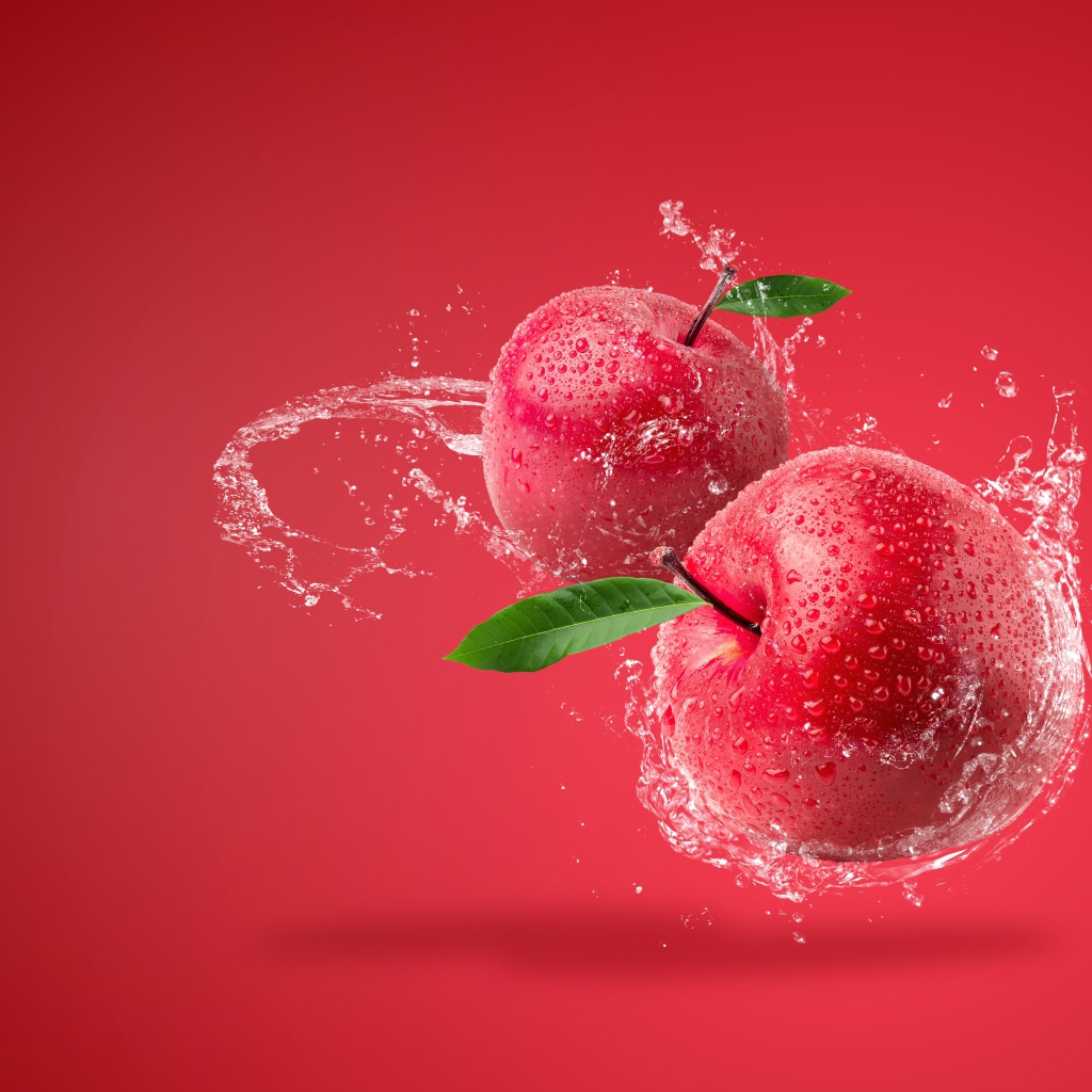 Два яблока в брызгах воды на красном фоне