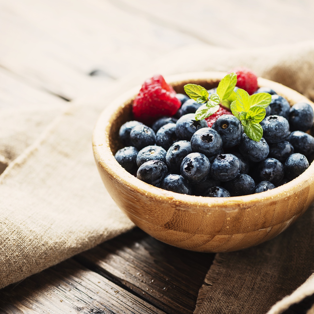 Мокрые ягоды черники в деревянной миске с малиной 