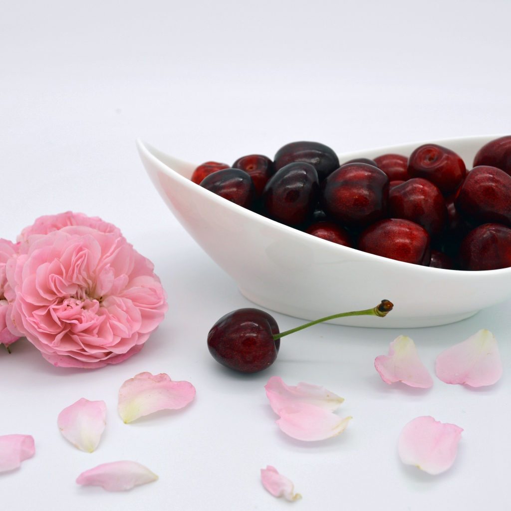 Белая тарелка с красными ягодами черешни на столе с цветами