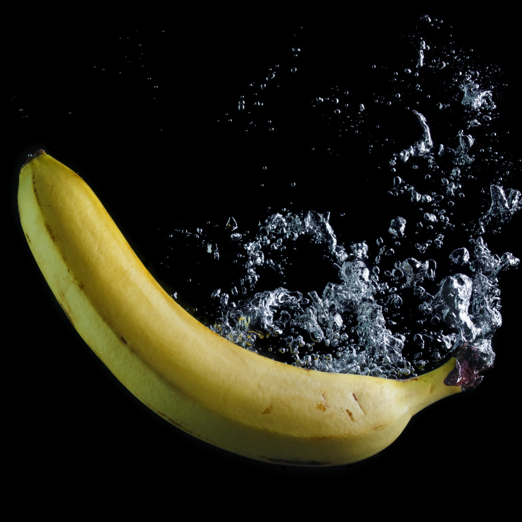 Желтый банан в воде на черном фоне