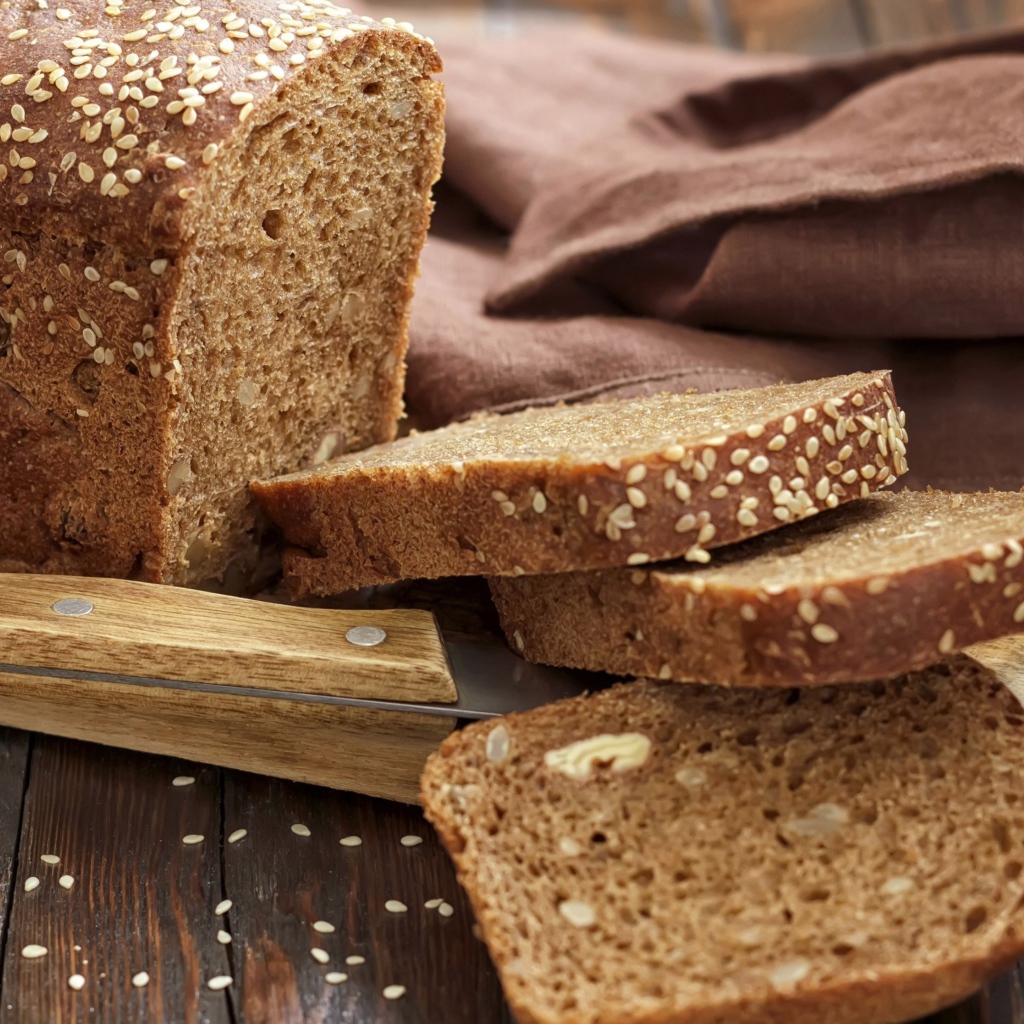 Буханка хлеба нарезанная кусочками на столе с ножом