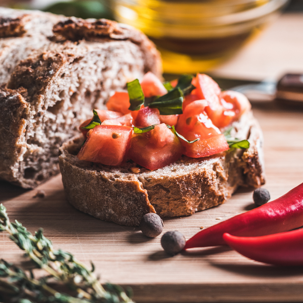 Черный хлеб с кусочками помидора на столе с острым красным перцем