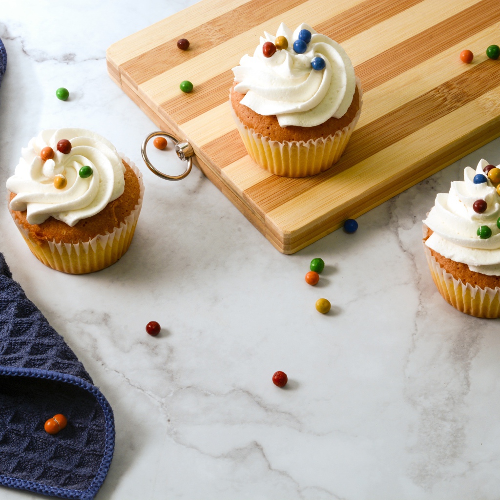 Кексы с кремом и разноцветными шариками на столе с доской