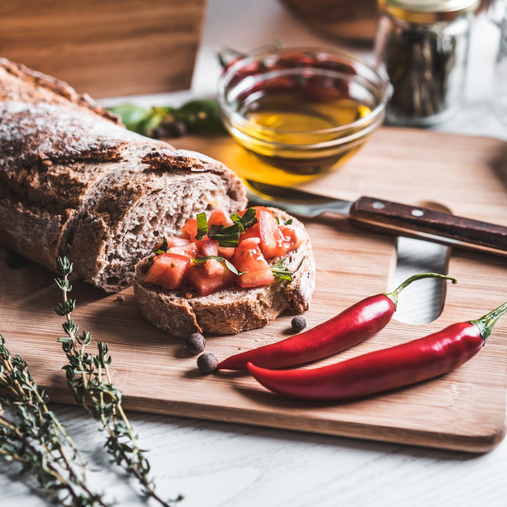 Батон с помидорами и красным перцем на столе с маслом