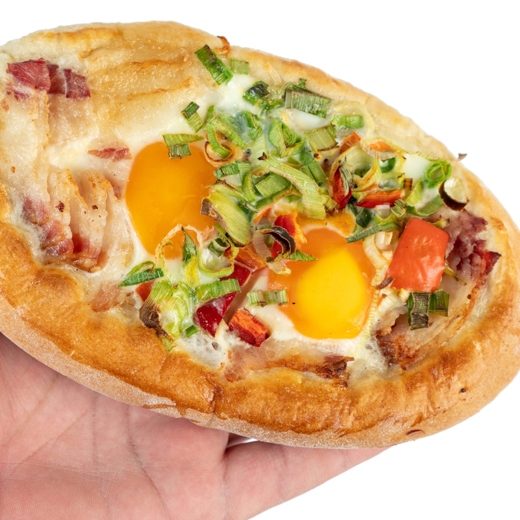 Вкусный свежий хачапури с яйцом и беконом в руке