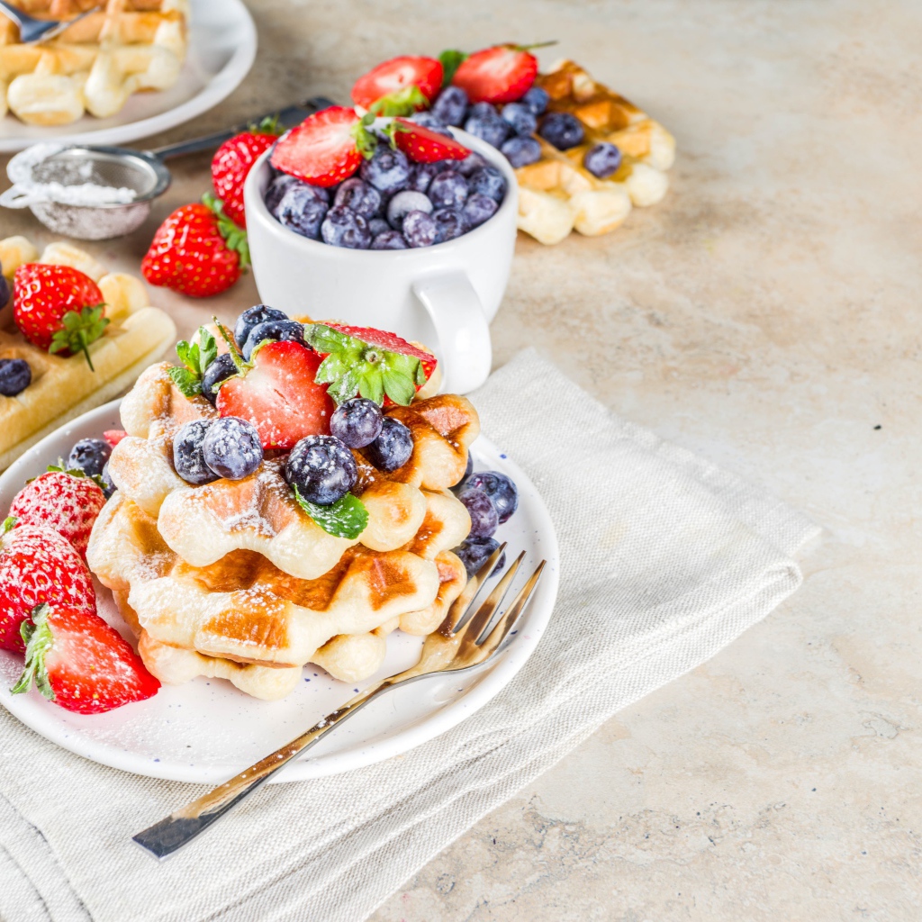 Вкусные сладкие вафли на тарелке с ягодами и сахарной пудрой 