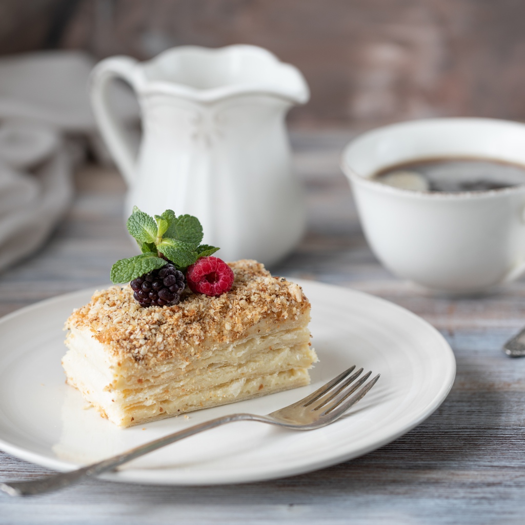 Кусок торта лежит на белой тарелке на столе с кофе