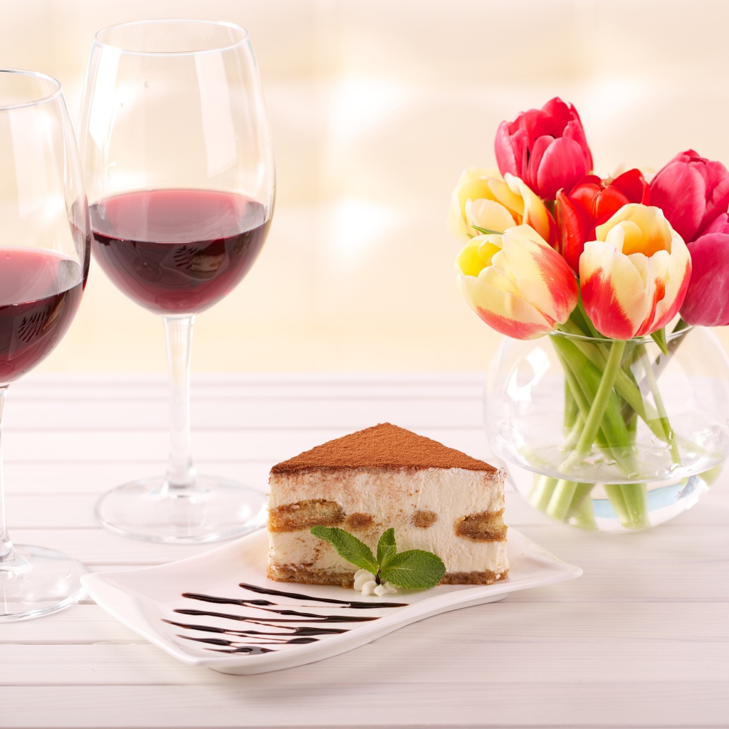 Кусок  тирамису на столе с бокалами вина и букетом тюльпанов