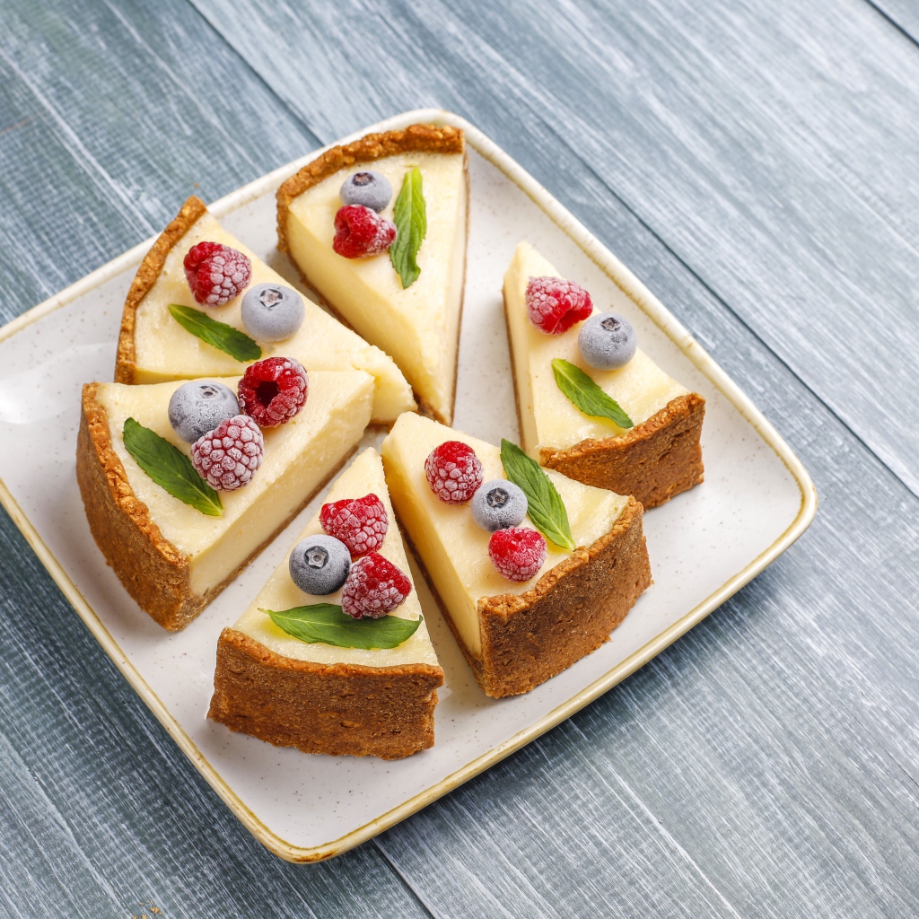 Аппетитный чизкейк с ягодами нарезан кусками на тарелке 