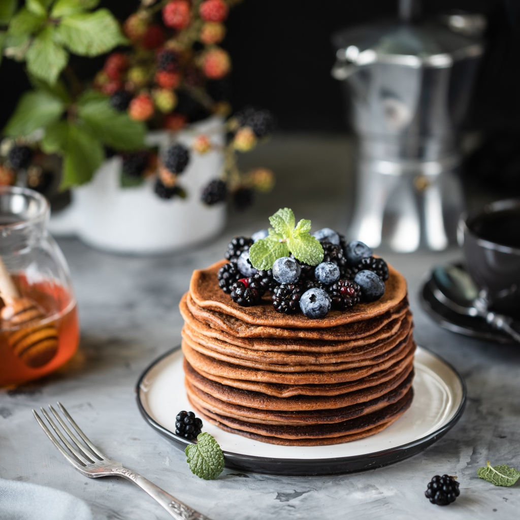 Гречневые блинчики с ягодами на столе с медом