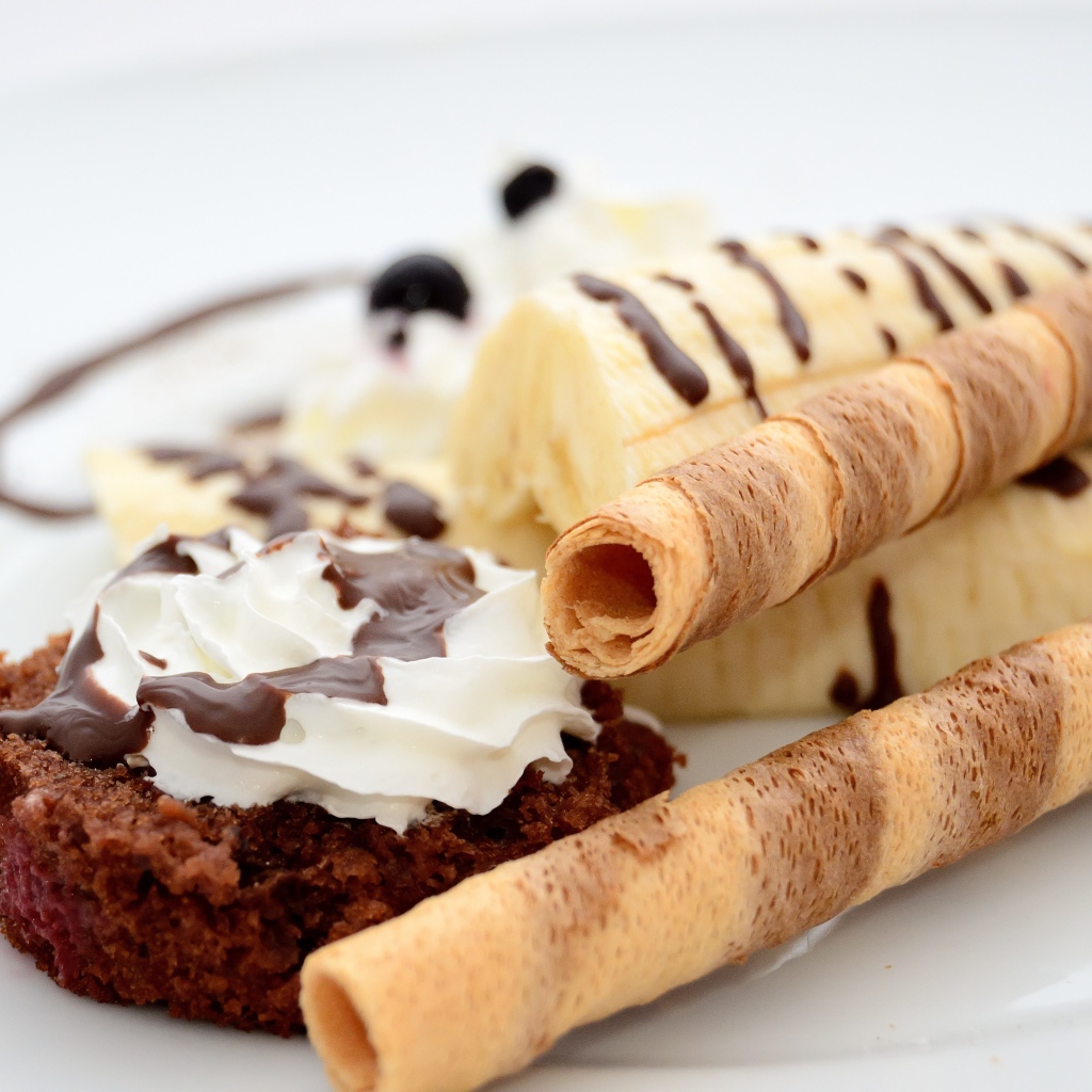 Пирожное на тарелке с бананом и сладкими трубочками