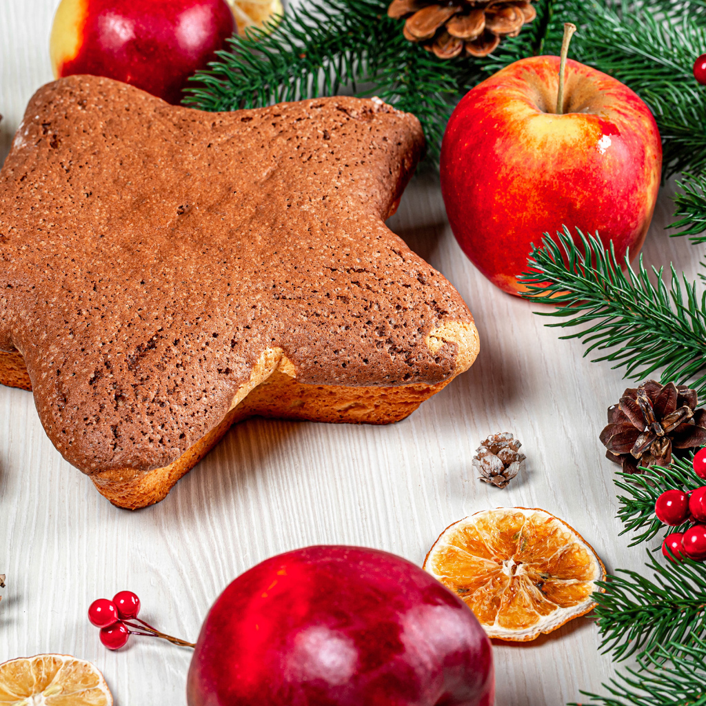 Рождественский кекс на столе с еловыми ветками,  яблоками и шишками