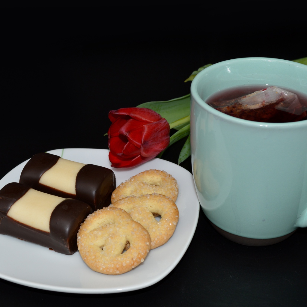 Печенье с конфетами на столе с чашкой чая и тюльпаном