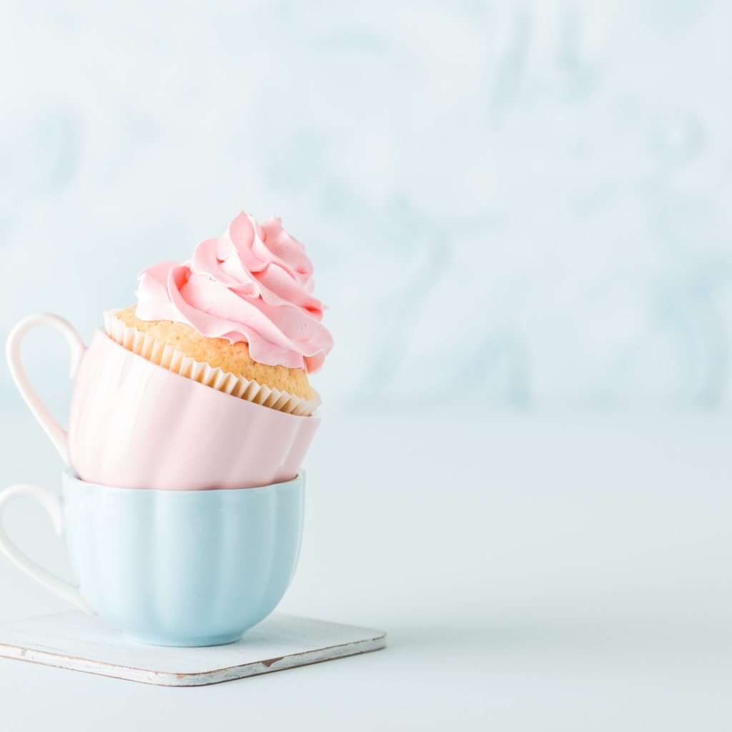 Кекс с розовым кремом с чашками на столе 