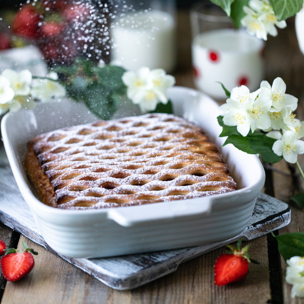 Вкусный клубничный пирог с сахарной пудрой на столе с цветами жасмина