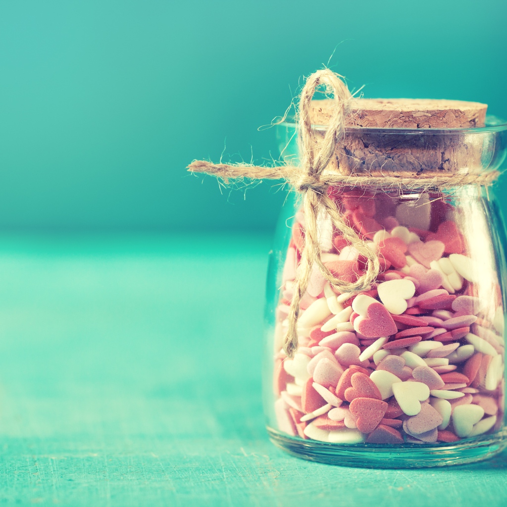 Стеклянная банка с маленькими конфетами в форме сердца на голубом фоне