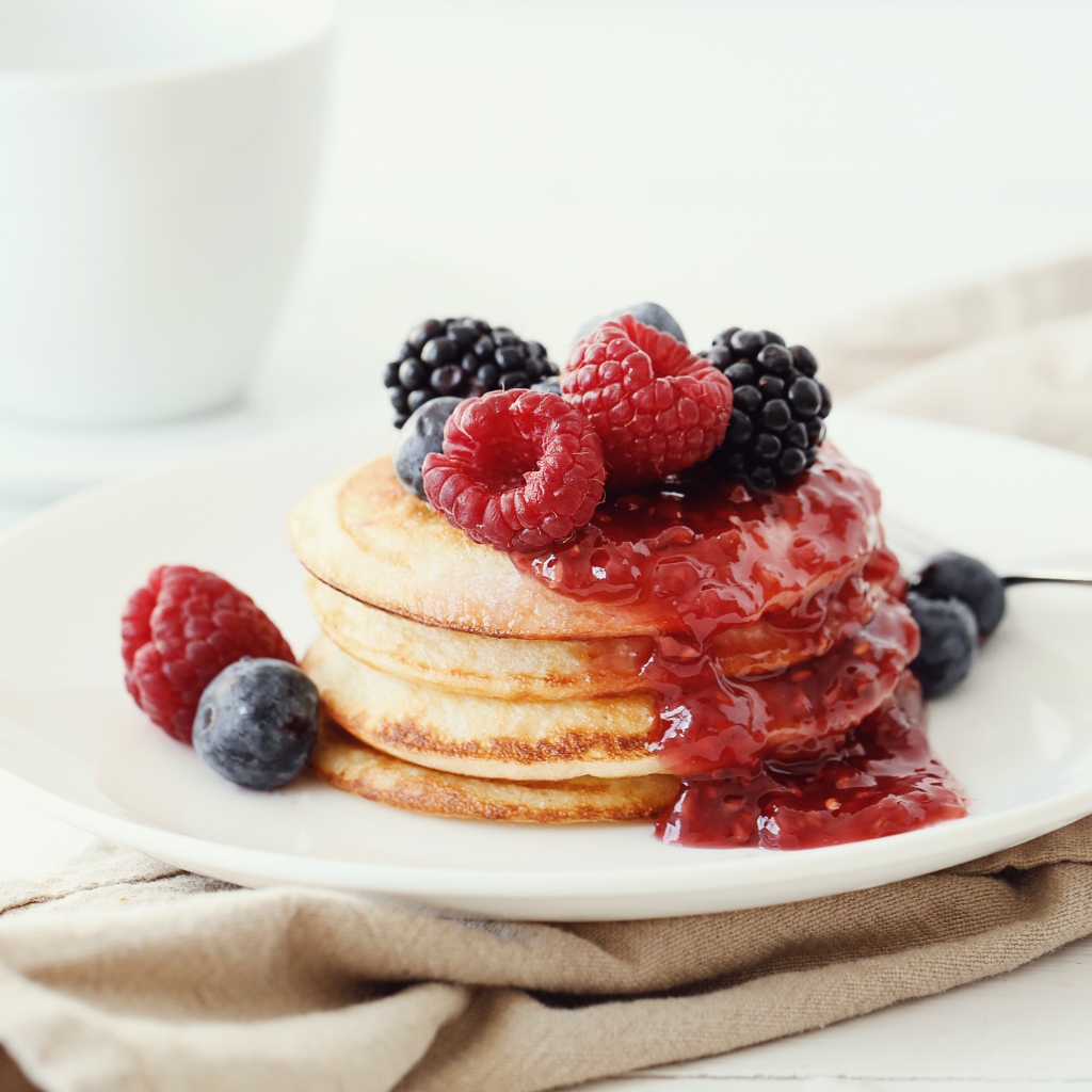 Оладьи на большой белой тарелке с джемом и ягодами 