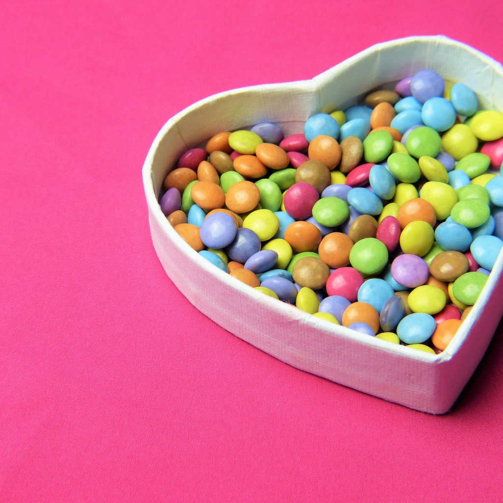 Коробка в форме сердца с разноцветными конфетами на розовом фоне