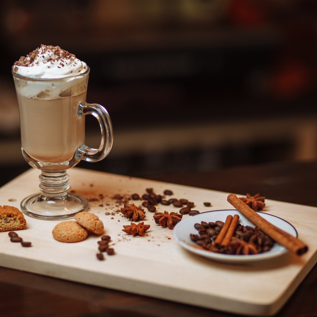 Горячее какао со сливками на столе с печеньем, зернами кофе и пряностями 