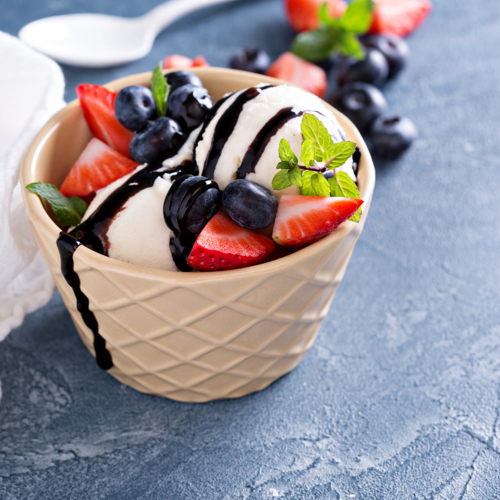 Шарики мороженого в стакане на столе с клубникой и ягодами черники