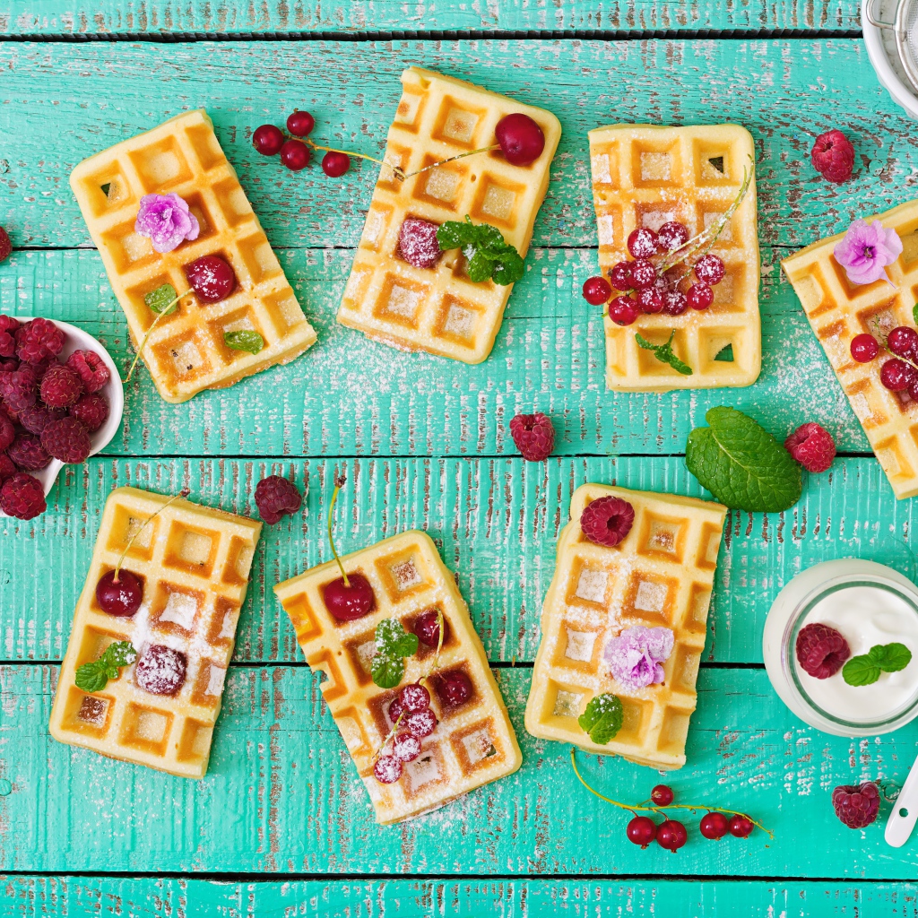 Большие сладкие вафли с ягодами и сахарной пудрой на столе 