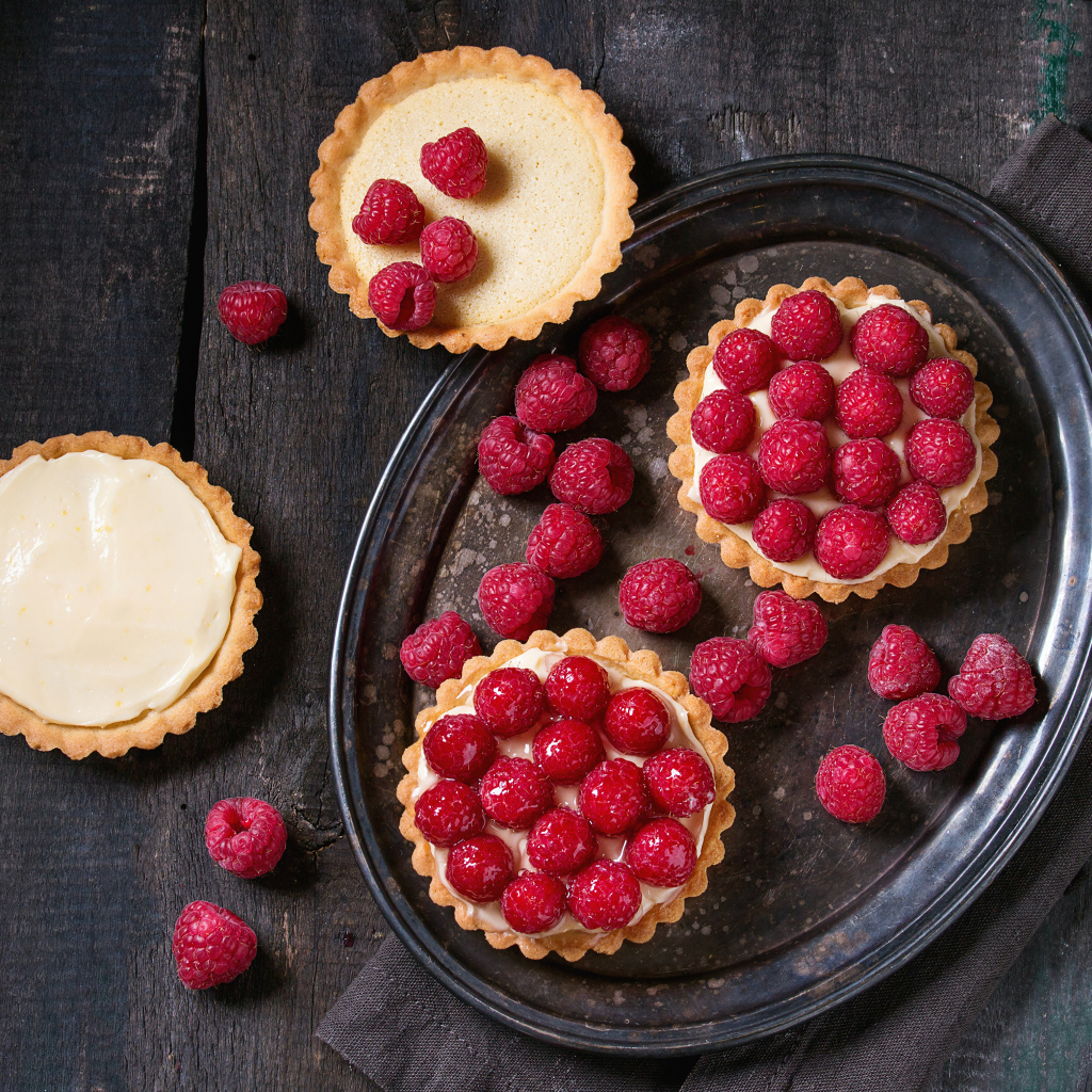 Кексы с кремом на блюде с малиной 