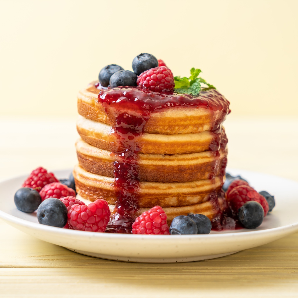 Румяные панкейки с джемом и ягодами черники и малины на тарелке