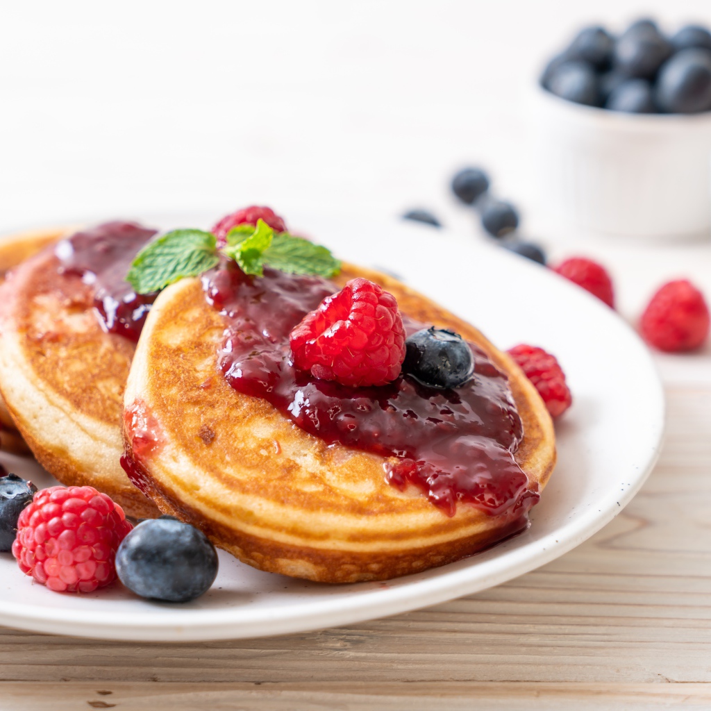 Румяные оладьи с джемом на тарелке с ягодами черники и малины