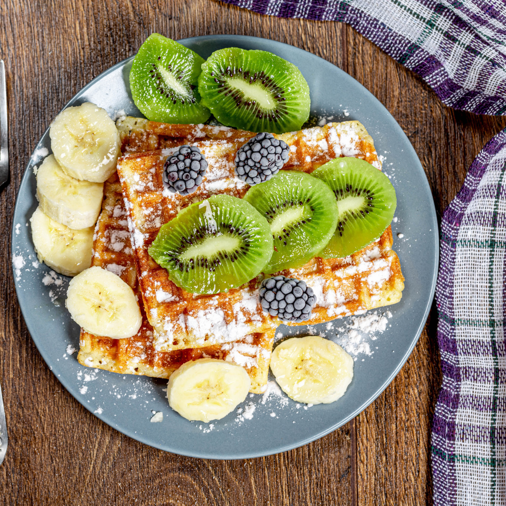 Сладкие вафли на тарелке с сахарной пудрой, бананами и киви