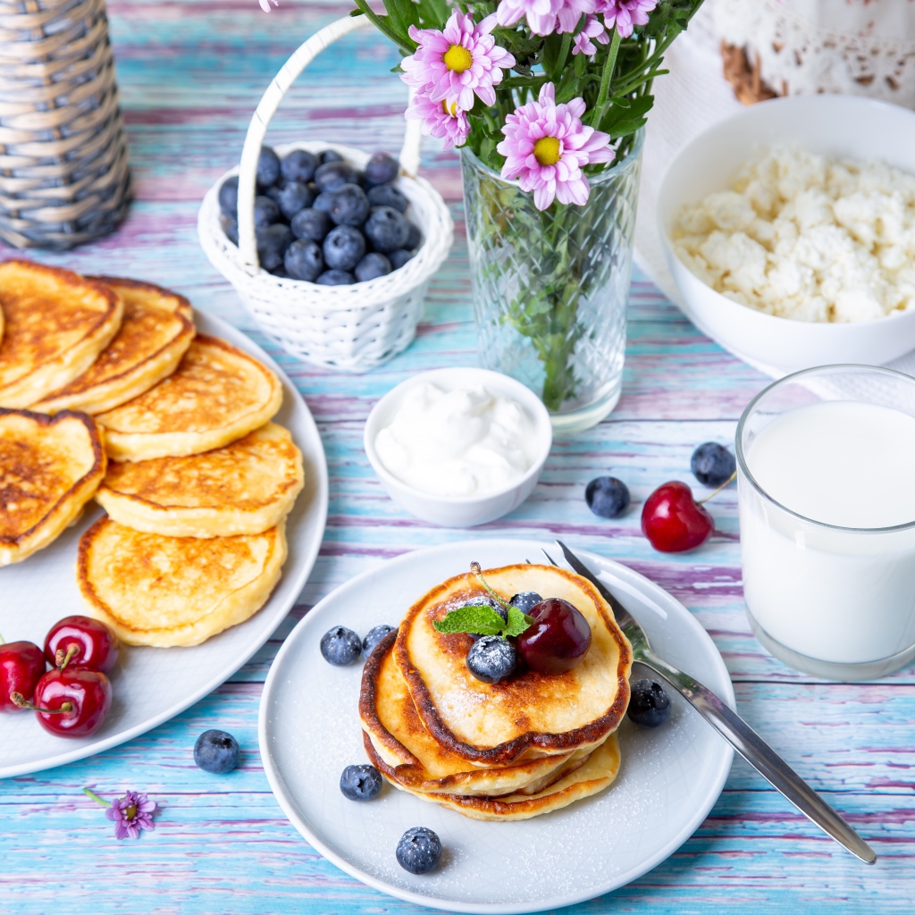 Вкусные оладьи на столе с ягодами черники, творогом и молоком